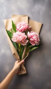 Man holding pink peonies bouquet in craft paper against white wall, free space for text