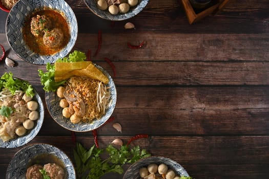 Top view of various spicy Thai noodles, scalded meatball and vegetables on wooden table.