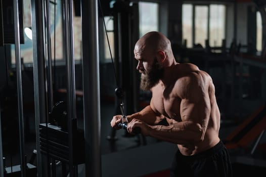 Bald Caucasian Bodybuilder doing heavy triceps exercises with cable