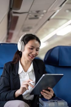 Businesswoman using tablet and headphones on airplane. Concept of in flight productivity and technology.