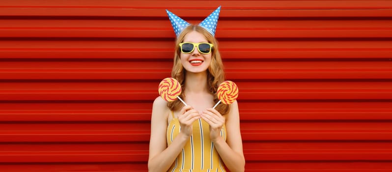 Holiday, celebration, event. Happy cheerful young woman laughs celebrating having fun at a party wearing festive birthday hat on red background