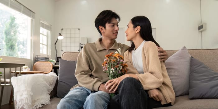 Young couple sitting together with flowers at home. Concept of love, affection, and intimacy.