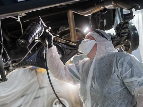 The master sprays an anti-corrosion compound on the bottom of the car