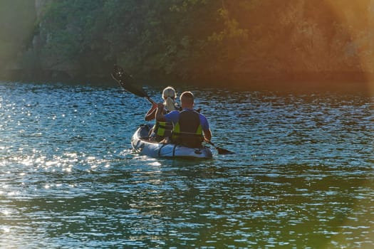 A young couple enjoying an idyllic kayak ride in the middle of a beautiful river surrounded by forest greenery in sunset time.