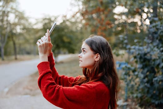 Woman in red sweater capturing scenic park view on cell phone