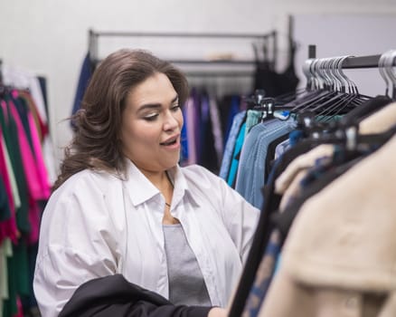 A fat woman in a plus size store chooses clothes while sorting through hangers