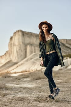 Woman in plaid shirt and hat standing in desert with majestic mountains in background