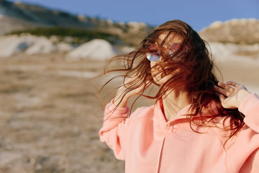 Serene woman in pink sweater standing in desert with hair blowing in wind