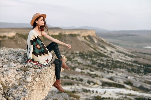 serene woman enjoying the view from mountain peak wrapped in a cozy blanket and wearing a hat
