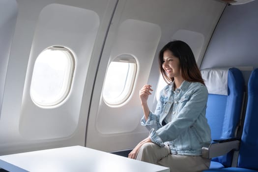 Asian woman smiling while sitting by airplane window. Concept of air travel, relaxation, and leisure.