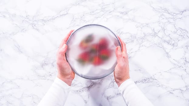 Flat lay. Strawberries, freshly washed and dried, are neatly stored in a glass bowl lined with a paper towel and securely covered with plastic wrap to maintain freshness.