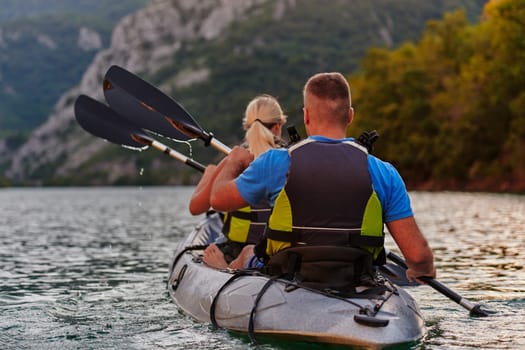 A young couple enjoying an idyllic kayak ride in the middle of a beautiful river surrounded by forest greenery in sunset time.