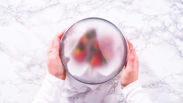 Flat lay. Strawberries, freshly washed and dried, are neatly stored in a glass bowl lined with a paper towel and securely covered with plastic wrap to maintain freshness.