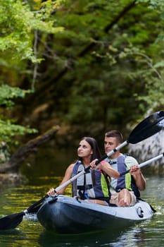 A young couple enjoying an idyllic kayak ride in the middle of a beautiful river surrounded by forest greenery.