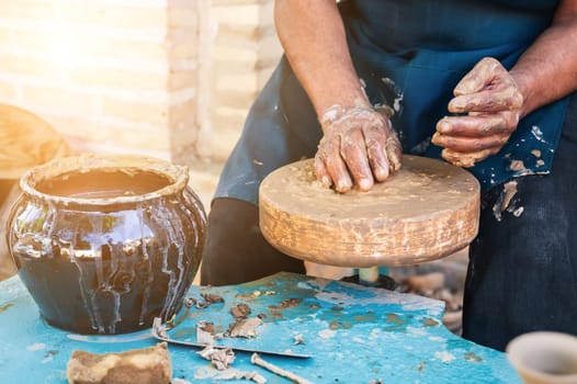 man artisan potter sculpts ceramic pottery from raw clay with hands on a machine in a pottery workshop in outdoor close up