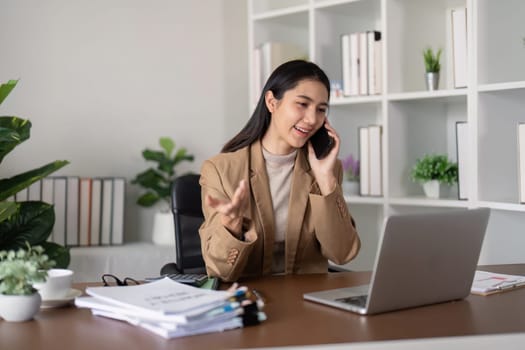 Smiling businesswoman on phone call at desk with laptop. Concept of professional communication and office work.