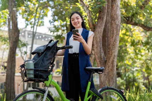 Business woman using smartphone next to bicycle in park. Concept of outdoor activities, technology, and healthy lifestyle.