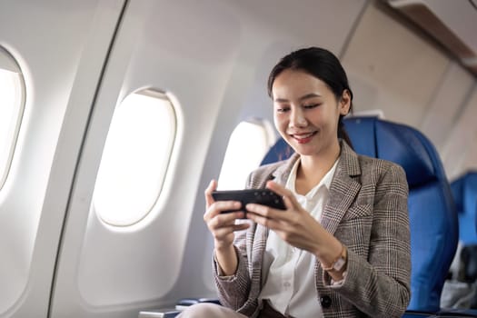 Smiling businesswoman using smartphone on airplane. Concept of in flight communication and business travel.