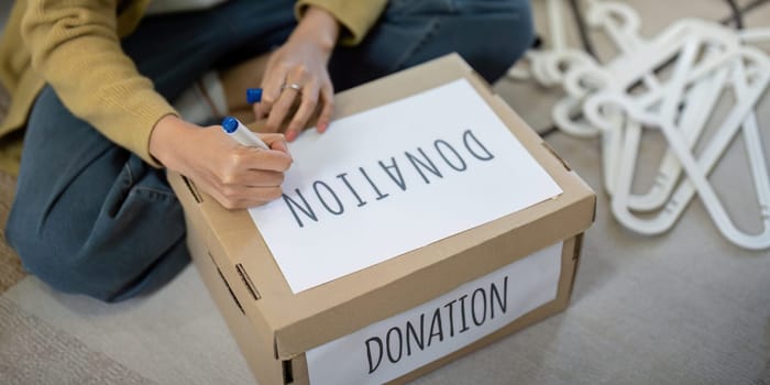 Close up of a person labeling a donation box at home. Concept of charity, giving, and community support.