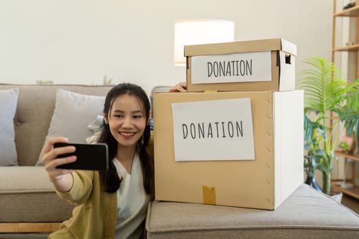 Woman taking selfie with donation boxes at home. Concept of charity, volunteering, and community support.