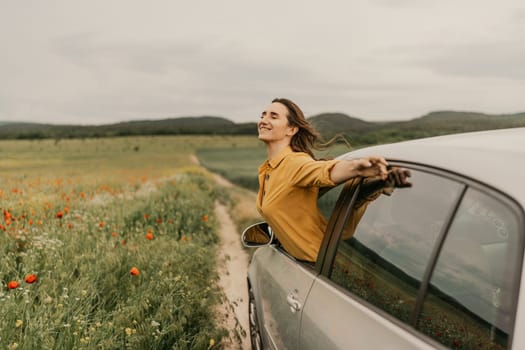 A woman is smiling and enjoying the view outside of a car. The scene is peaceful and serene, with a beautiful field of flowers in the background. The woman is leaning out of the car window