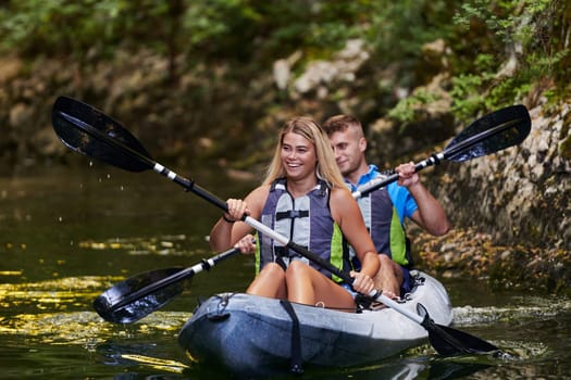 A young couple enjoying an idyllic kayak ride in the middle of a beautiful river surrounded by forest greenery.