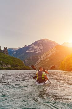 A young couple enjoying an idyllic kayak ride in the middle of a beautiful river surrounded by forest greenery in sunset time.