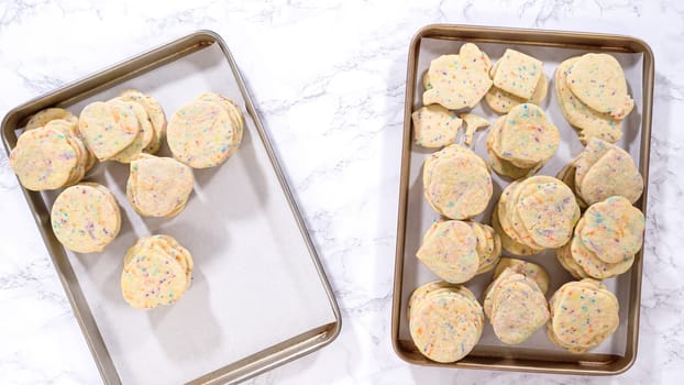 Flat lay. With precision, the woman is carefully arranging the sugar cookies, filled with dough-mixed sprinkles, into a rustic brown paper box.