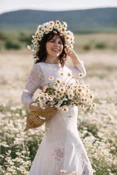 Happy woman in a field of daisies with a wreath of wildflowers on her head. woman in a white dress in a field of white flowers. Charming woman with a bouquet of daisies, tender summer photo.