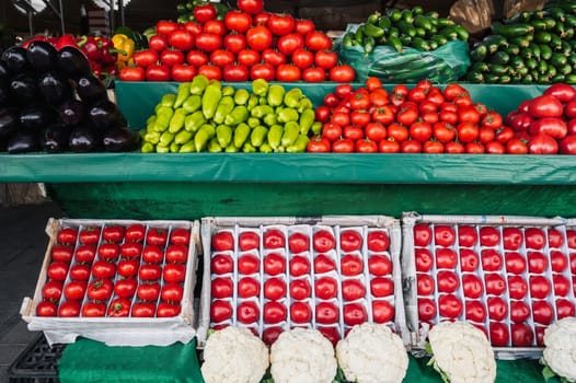 counter with an assortment of fresh vegetables at a grocery farmers market. Tomatoes, cucumbers, cauliflower, peppers and eggplant on store shelves