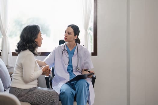 Doctor consulting with senior woman on sofa in home. Healthcare and patient support concept.