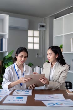 Businesswomen collaboration on financial documents at office desk. Concept of teamwork, analysis, and professional discussion.