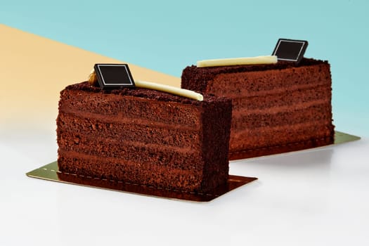 Pair of delicious rich layered chocolate cake slices coated with crispy streusel, presented on gold bases against pastel blue and yellow background