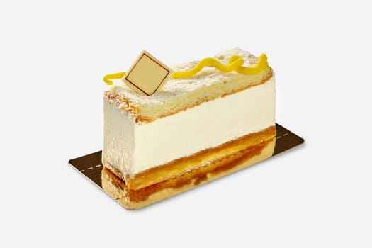 Light dessert of creamy mousse between layers of soft vanilla sponge cake decorated with branded chocolate plaque and yellow swirl, presented on golden cardboard base