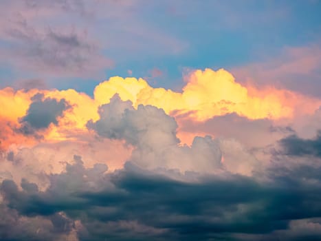 Warm hues of orange and pink illuminate soft, fluffy clouds as the sun sets over a peaceful countryside. The contrasting dark and light clouds create a stunning visual spectacle against the vibrant evening sky.