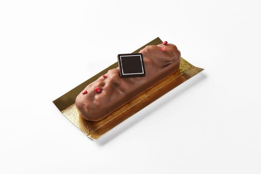 Appetizing milk chocolate bar with pecan decorated with dried berry crumbs and branding dark chocolate plaque on golden cardboard, against white background