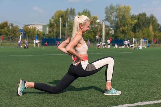 Young sporty woman in sportswear stretching on stadium