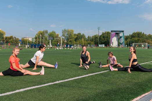 Female coach and group of children conducts a training session at the stadium outdoors