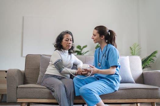 Caregiver measuring blood pressure of senior woman on sofa in home. Healthcare and patient monitoring concept.