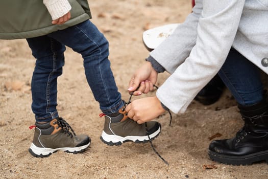 Close up of mother helping her child tying the shoes.