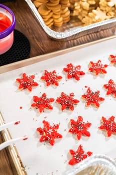 Vivid red star-shaped cookies, generously iced and speckled with green and white holiday sprinkles, freshly prepared and laid out to dry.