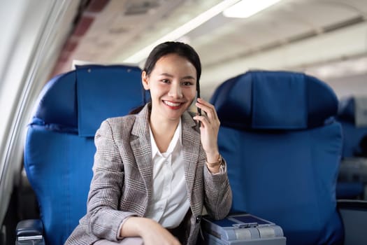 Smiling businesswoman on airplane talking on phone. Concept of in-flight communication and business travel.