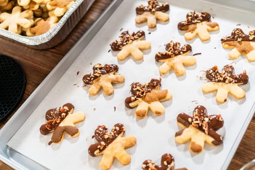 Creating snowflake-shaped cutout sugar cookies, dipped in chocolate, and adorned with crushed pecan nuts, elegantly presented on parchment.