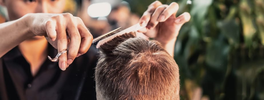 Neat young Vietnamese hairdresser makes haircut to male. Back view. Professional skills.