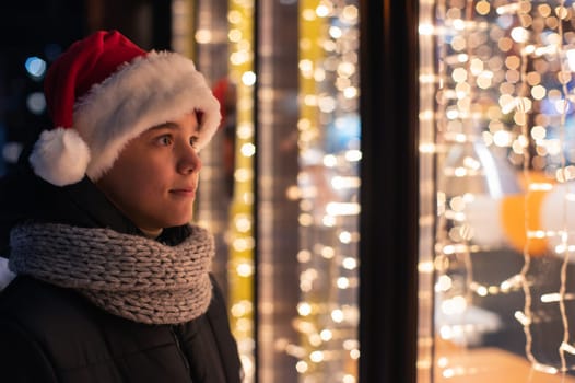 Teen Boy in Santas hat looking and dreaming in illuminated shop window. Xmas presents holidays, or shopping on New Year or Christmas concept