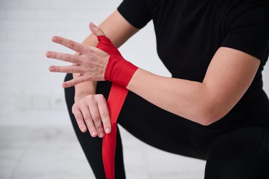 Selective focus on hands of female fighter preparing for boxing competition challenge training, tying tapes before putting boxing gloves, isolated over white background. Sport and martial art concept.