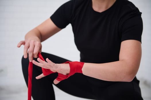 Closeup selective focus on the hands of a woman tying tape around her hand, before getting boxing gloves preparing to boxing practice.