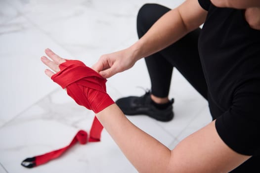 Top view of an Caucasian boxer fighter woman in black sports wear, tying tape around her hand before get boxing gloves preparing to boxing practice.