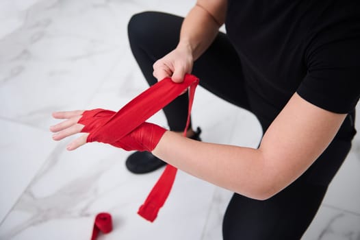 Top view of an European boxer fighter woman in black sports wear, tying tape around her hand before get boxing gloves preparing to boxing practice. Martial art and combat concept