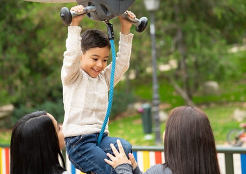 Excited young boy hanging on a zip line with his lesbian mothers.